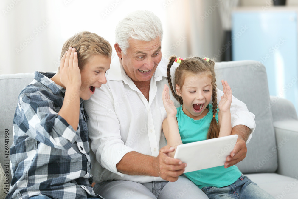 Fototapeta premium Grandfather and grandchildren with tablet on couch