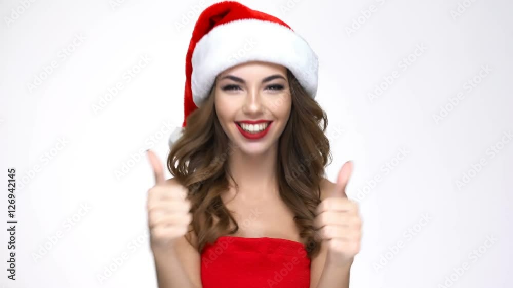 Cheerful beautiful young woman in santa claus hat showing thumbs up Cheerful beautiful young woman in santa claus hat showing thumbs up
