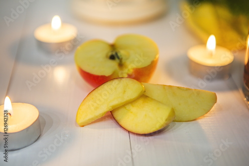 Половина яблока, дольки яблока и свечи на белом деревянном столе. 