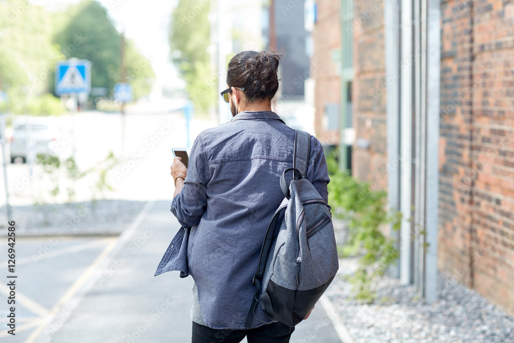 man with backpack and smartphone walking in city