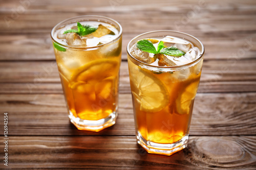 Glasses of iced tea with lemon slices and mint on wooden background