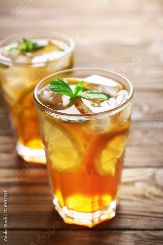 Glass of iced tea with lemon slices and mint on wooden background, closeup