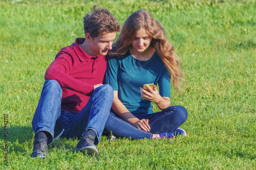 Couple teenagers sitting on the green lawn with a smartphone