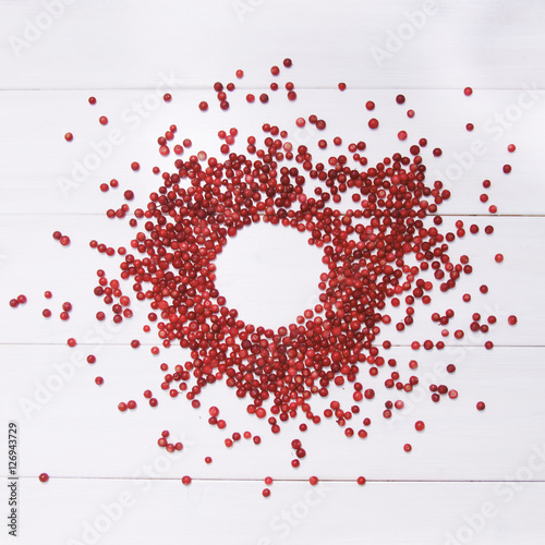 Round frame of red cranberries on white wooden background