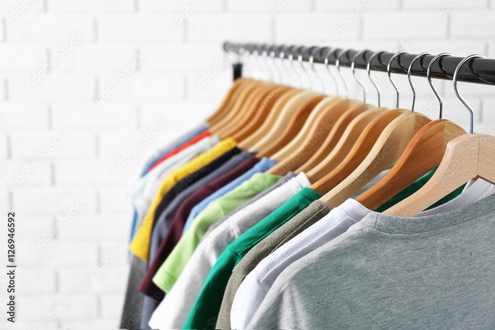 Obraz premium Colorful t-shirts on hangers against light blurred background, close up view