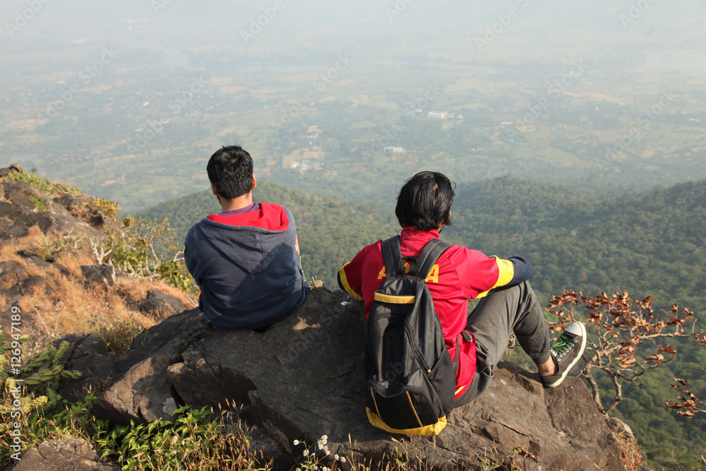 Two Young boys with backpack taking sitting on the top of a mountain ...