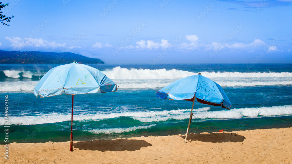 tropical beach with big waves and two umbrellas in the sand