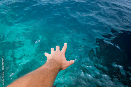 Hand of a young caucasian male appearing to touch the surface of amazing blue water of the Indian Ocean. 