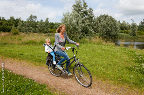 Happy grandmother with grandchild cycling towards you in nature