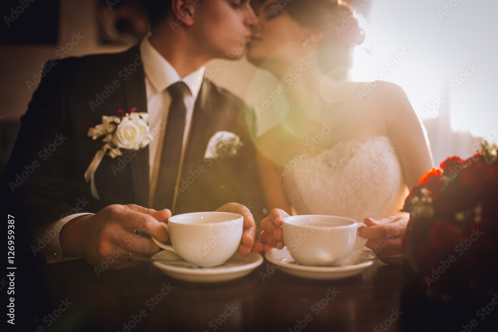 Bride and groom drinking coffee at cafe after their wedding. Posing and embracing newlyweds.