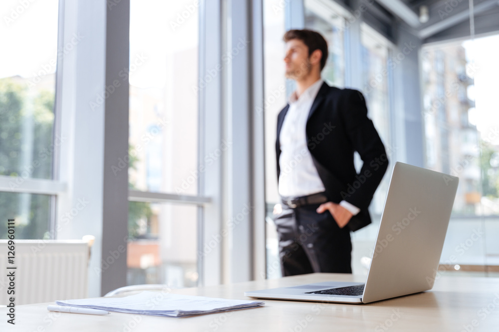 Businessman with laptop and documents standing near the window Businessman with laptop and documents standing near the window