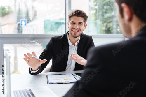 Two happy young businessmen sitting and working on business meeting