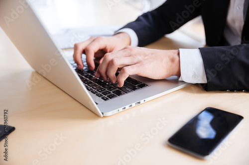 Hands of businessman using laptop and blank screen cell phone