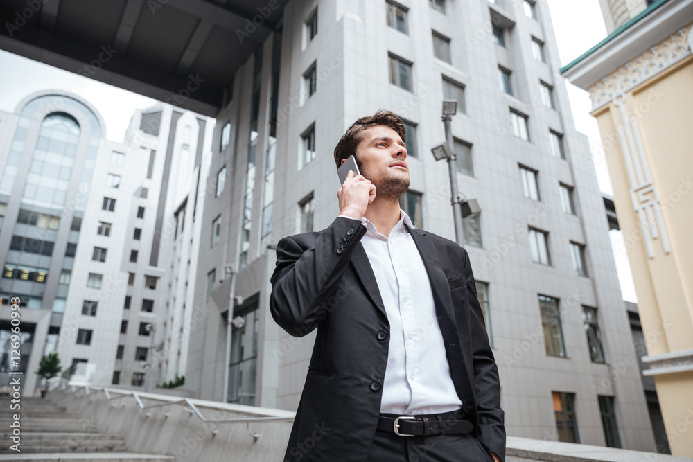 Serious young businessman talking on cell phone near business center Serious young businessman talking on cell phone near business center
