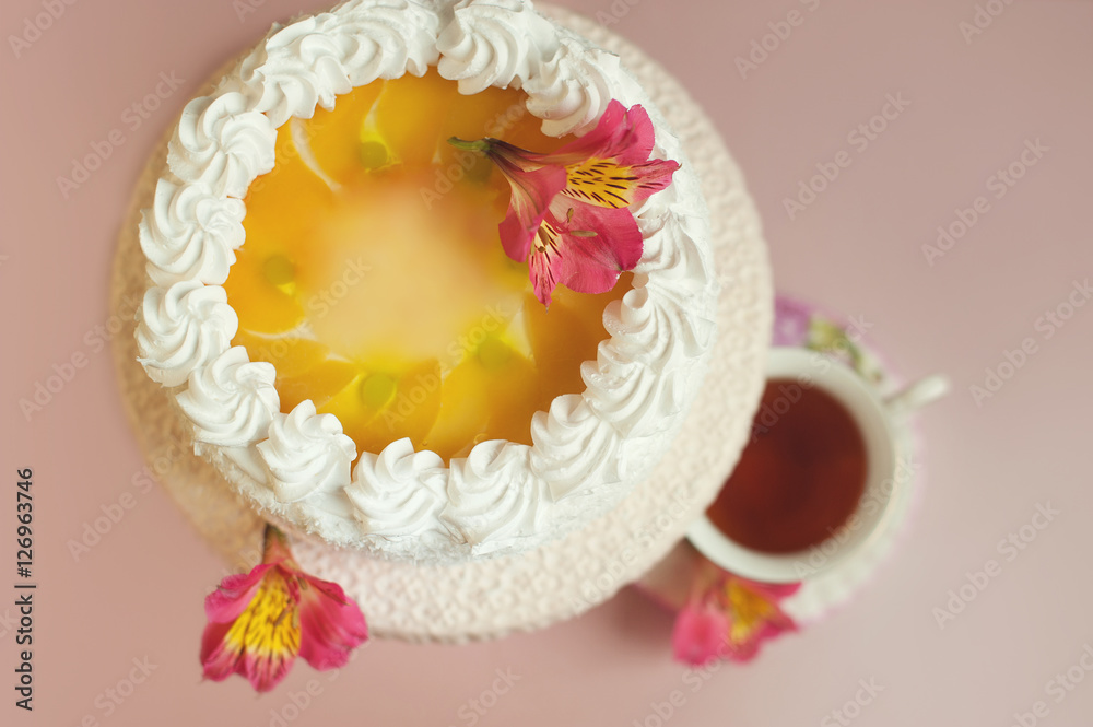Homemade cake with yellow jelly decorated white creamcup on pink table. Top view. Cup of tea the blurred background. Shallow focus. Homemade cake with yellow jelly decorated white creamcup on pink table. Top view. Cup of tea the blurred background. Shallow focus.