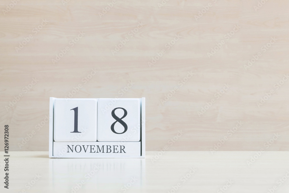 Closeup surface white wooden calendar with black 18 november word on blurred brown wood desk and wood wall textured background with copy space , selective focus at the calendar Closeup surface white wooden calendar with black 18 november word on blurred brown wood desk and wood wall textured background with copy space , selective focus at the calendar