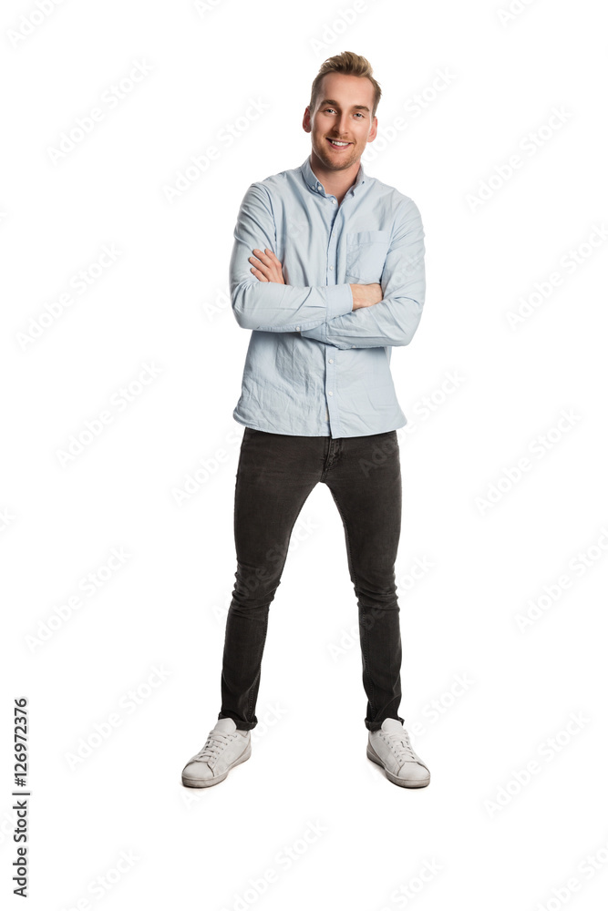 A handsome man in his 20s standing against a white background, smiling, wearing a blue shirt and grey jeans. A handsome man in his 20s standing against a white background, smiling, wearing a blue shirt and grey jeans.