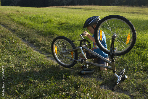 Preteen boy repair bicycle  on the summer sunny park
