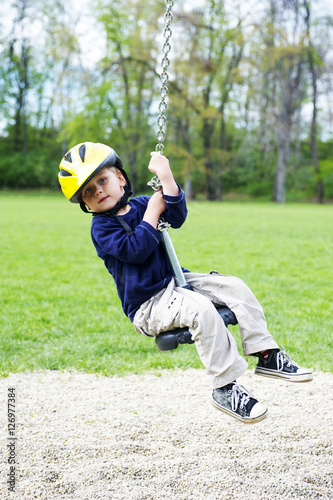 Cute child, boy wearing the bike helmet, rides on Flying Fox play equipment in a children's playground, summertime