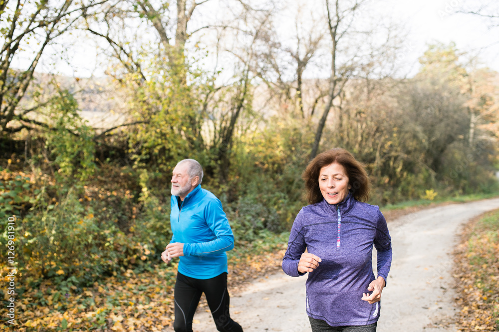 Beautiful senior couple running outside in sunny autumn forest Beautiful senior couple running outside in sunny autumn forest