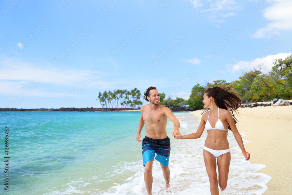 Happy couple laughing together holding hands running having fun splashing water in the ocean waves. Young beautiful fit slim body people enjoying their happy lifestyle in paradise destination beach. Happy couple laughing together holding hands running having fun splashing water in the ocean waves. Young beautiful fit slim body people enjoying their happy lifestyle in paradise destination beach.