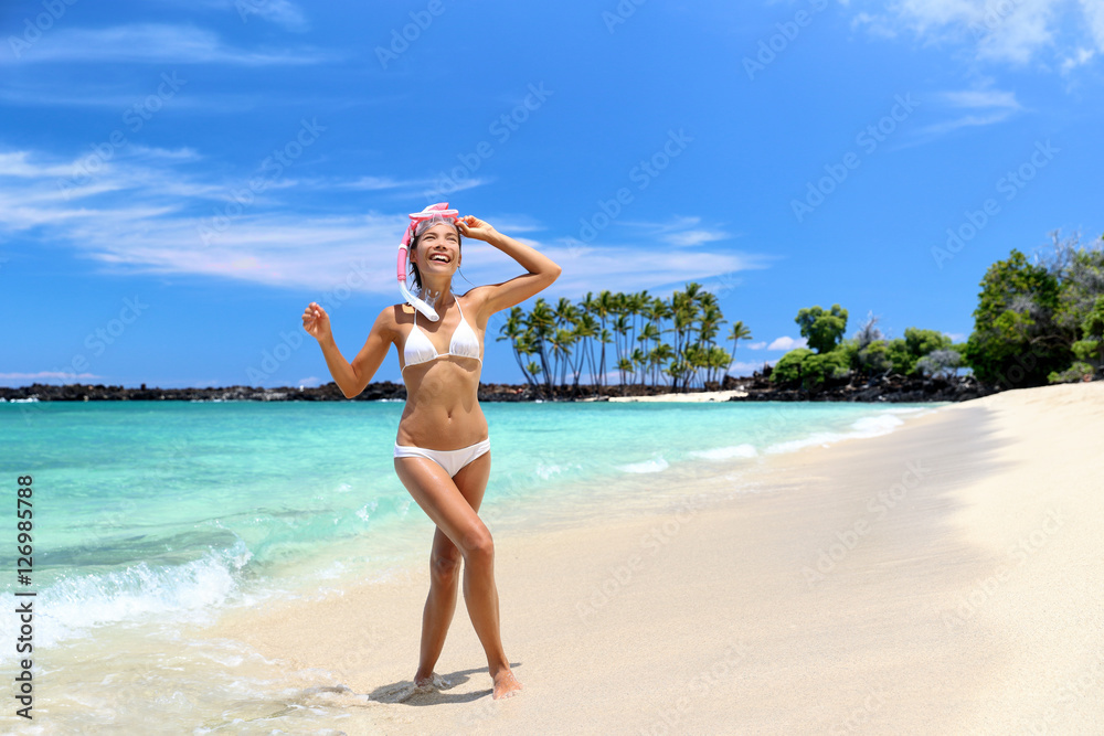 Beach vacation woman enjoying swimming coming out of turquoise ocean water walking with snorkel mask relaxing on perfect white sand travel destination. Asian bikini girl happy for relaxation holiday.