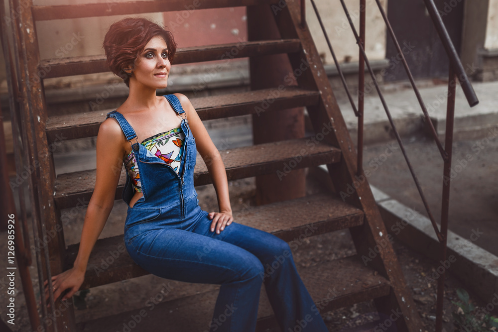 urban young woman sit on iron stairs in blue jeans in brutal pose, unusual toned shot