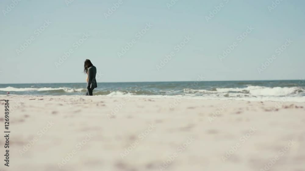 A dark-haired pregnant woman is having a peaceful walk along the sea shore on a windy day. A dark-haired pregnant woman is having a peaceful walk along the sea shore on a windy day.