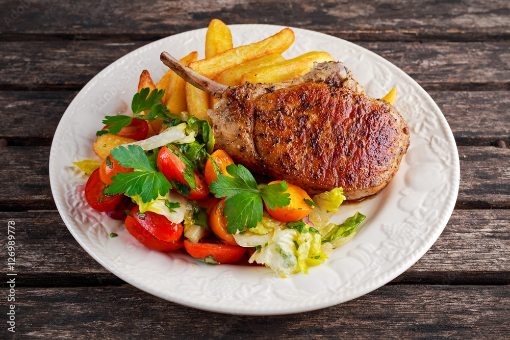 Grilled pork cutlet meat garnished with potato and salad on a wooden table. Grilled pork cutlet meat garnished with potato and salad on a wooden table.