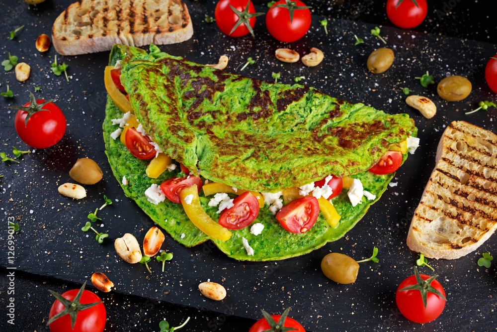 Vegetables Green Omelette with tomatoes, greek cheese, olives, nuts, paprika, toast on stone background. concept healthy food.