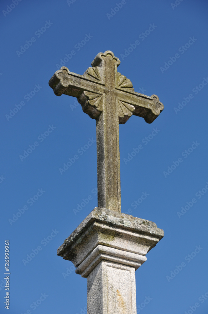 Steinkreuz auf Säule vor blauem Himmel