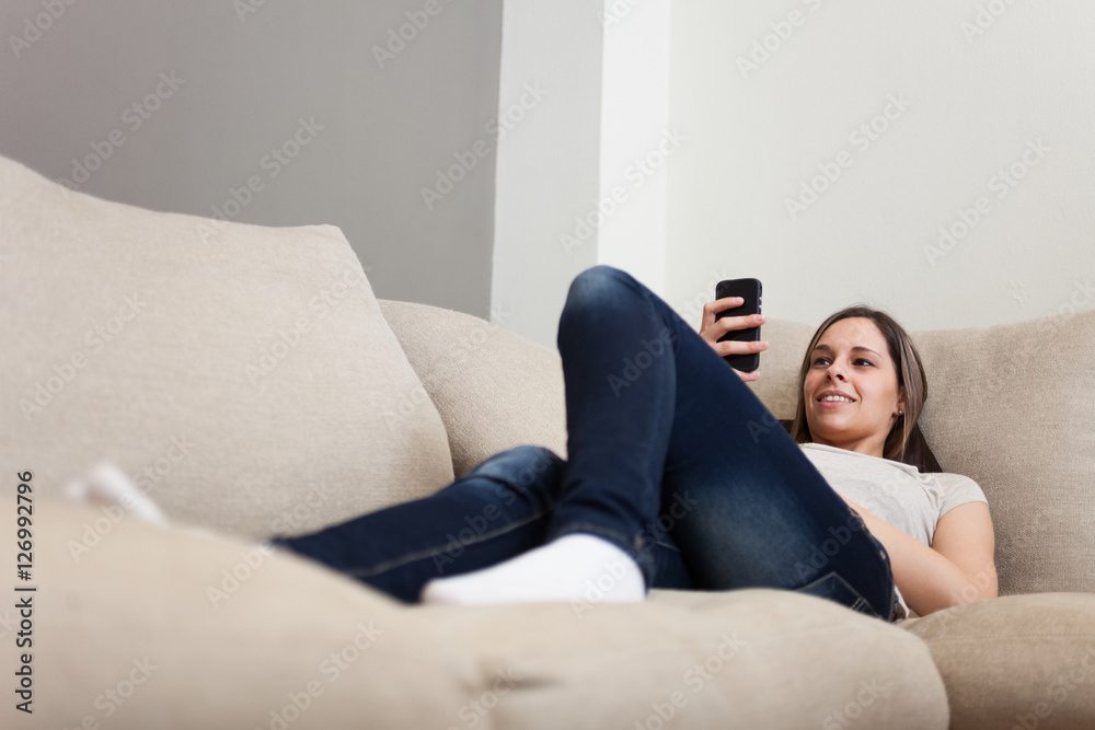 Woman sitting on a couch in her apartment while using her mobile phone Woman sitting on a couch in her apartment while using her mobile phone
