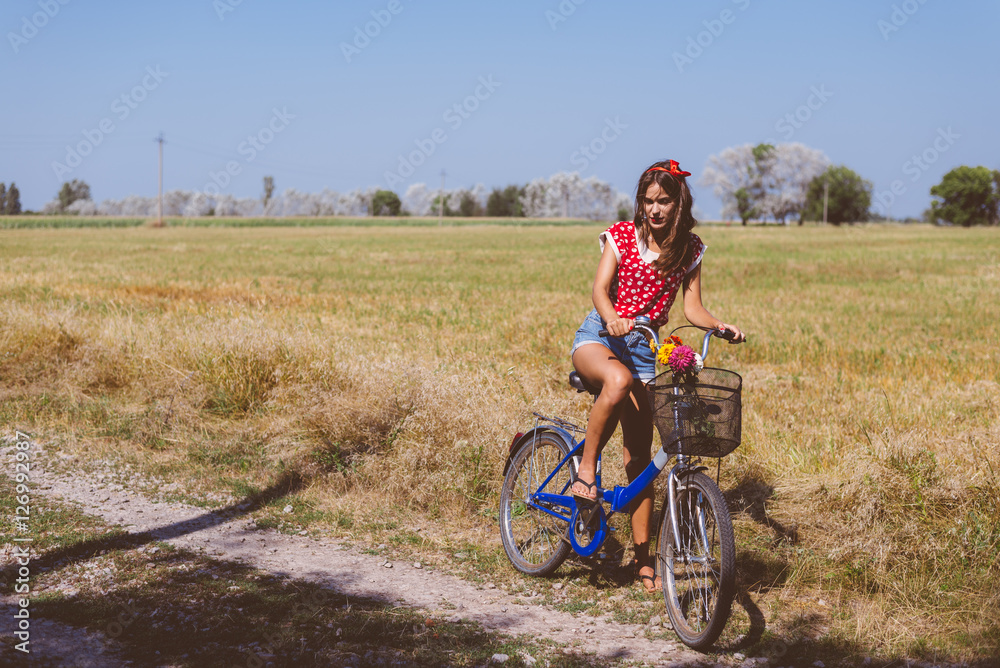 Young pinup woman cycling in fields under bright blue summer sky copy space image