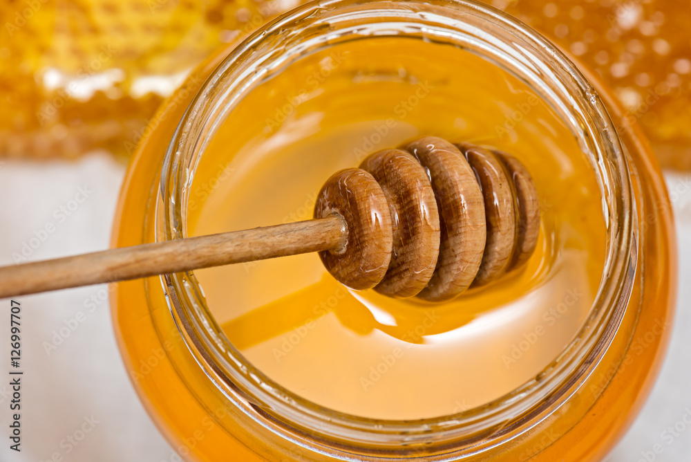 Honey on dipper in jar and   bee honeycomb background