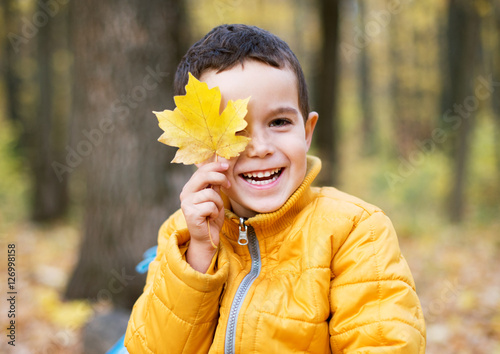 Cheerful boy smiling and hiding behind yellow leaf