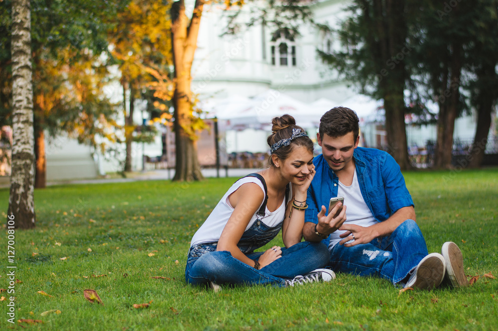 Love couple at the park. Looking at mobile and smiling.
