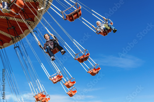Fényképezés Mother with the six-year-old son ride an attraction on a swing agains the blue s