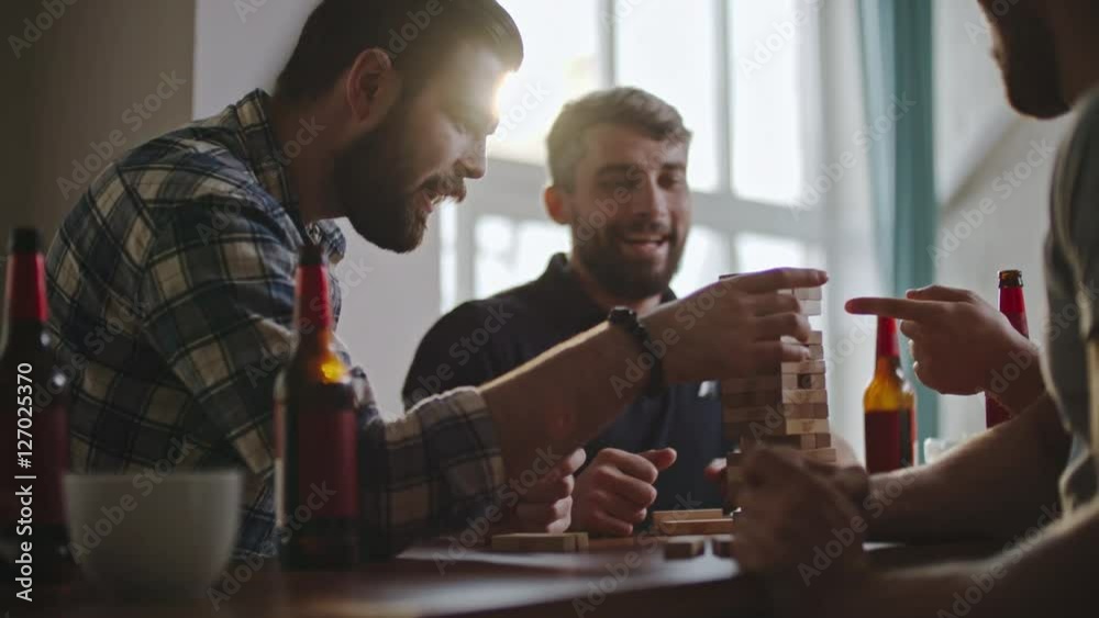 Bearded man carefully removing wooden block from jenga tower while playing with friends at party