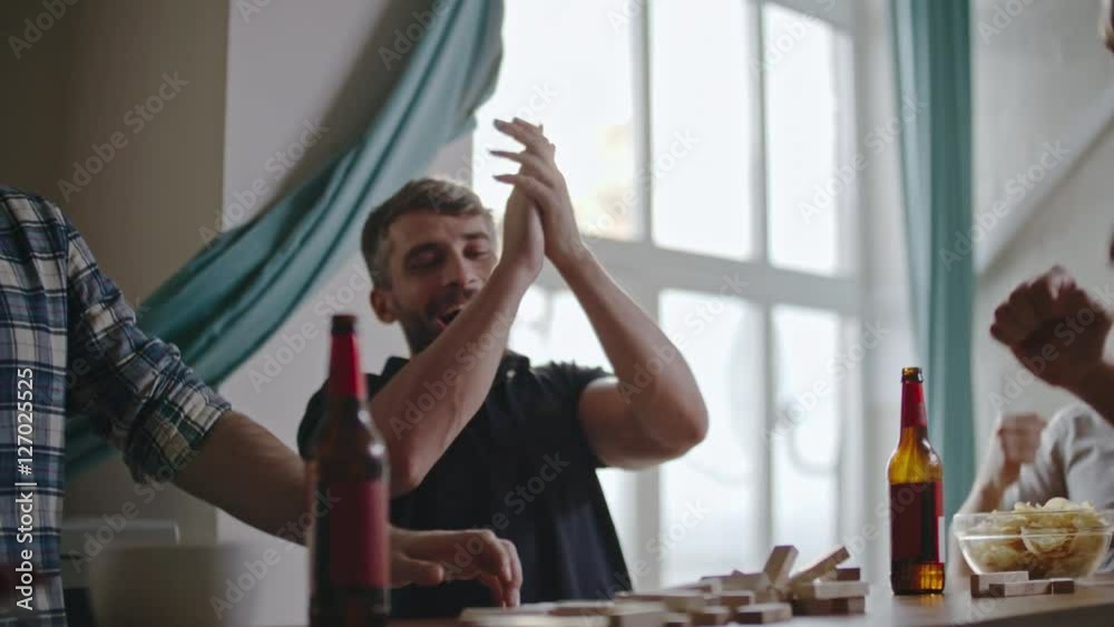 Guys laughing and high-fiving each other as their friend making jenga tower fall by accident