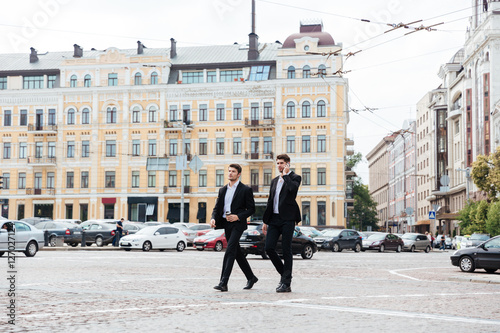 Two businessmen walking and talking on cell phone in city
