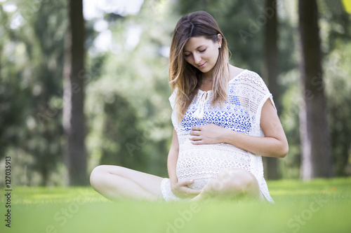 Pregnant woman in the park looking at her belly and smiling