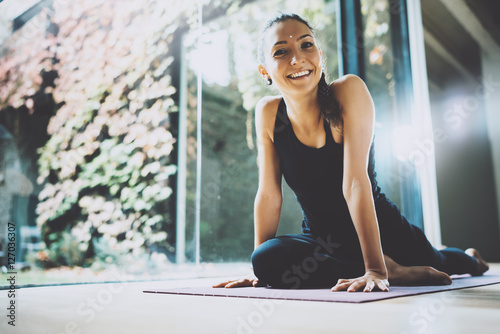 Portrait of gorgeous young woman practicing yoga indoor. Beautiful girl smiling during practice class.Calmness and relax, female happiness concept.Horizontal, blurred background.