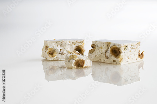 torrone alle nocciola a pezzi su fondo bianco con riflesso in primo piano