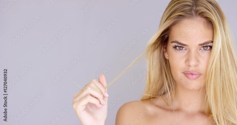 Seductive blond woman twirling her long hair in her fingers as she gives the camera a sultry look close up cropped head shot on grey with copy space. Seductive blond woman twirling her long hair in her fingers as she gives the camera a sultry look close up cropped head shot on grey with copy space.