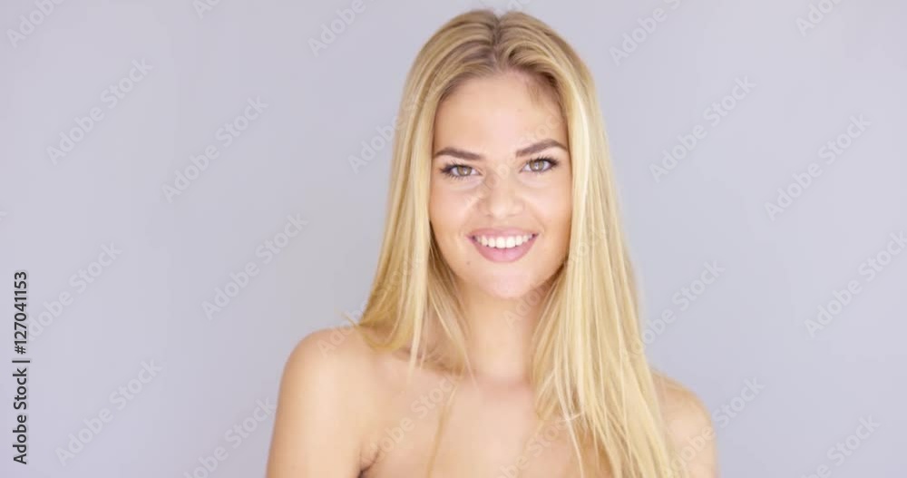 Beautiful happy girl smiling to the camera. It is close up on her face with big smile and white teeth. She has bare shoulders and long blond hair. Isolated on gray background Beautiful happy girl smiling to the camera. It is close up on her face with big smile and white teeth. She has bare shoulders and long blond hair. Isolated on gray background