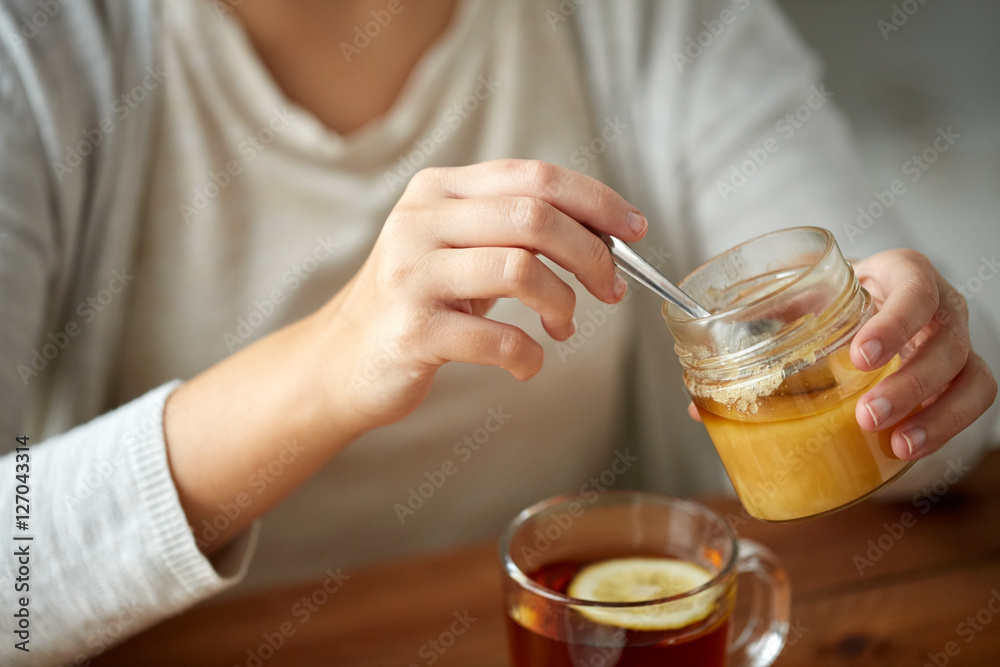 close up of woman adding honey to tea with lemon close up of woman adding honey to tea with lemon