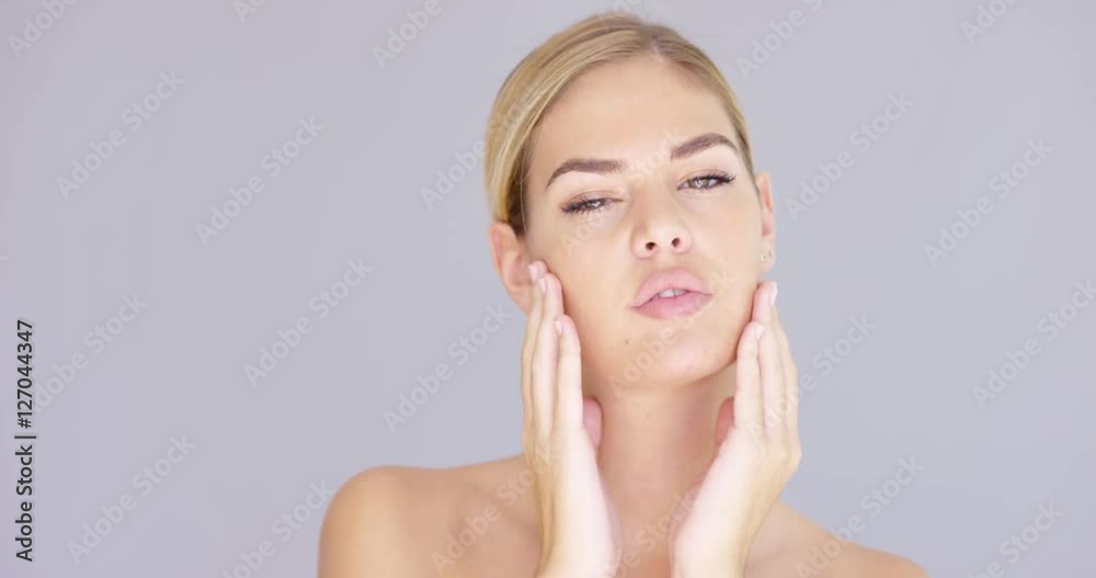 Young caucasian blond girl posing over gray background. She has bare shoulders touching cheeks with her hands. Natural look. Simple purity. Isolated. Young caucasian blond girl posing over gray background. She has bare shoulders touching cheeks with her hands. Natural look. Simple purity. Isolated.
