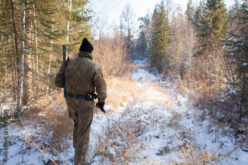 a hunter in the winter woods with a gun in camouflage clothing.