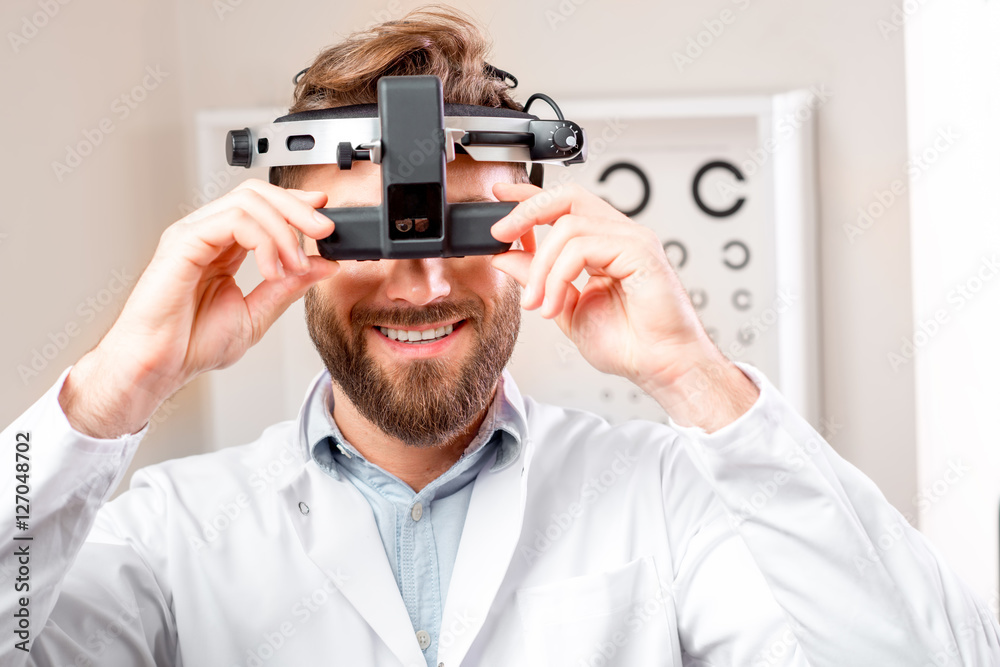 Eye doctor with ophthalmologic binocular device for checking vision with the eye chart on the background in the cabinet Eye doctor with ophthalmologic binocular device for checking vision with the eye chart on the background in the cabinet