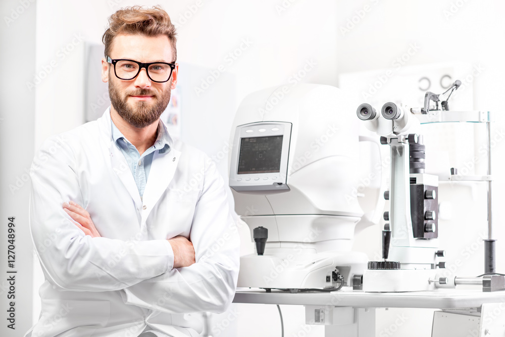 Portrait of handsome eye doctor sitting with ophthalmologic device in the cabinet Portrait of handsome eye doctor sitting with ophthalmologic device in the cabinet